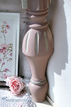 a pink vase sitting on top of a white shelf next to a framed photo and flower