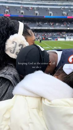 two women in black and white hats hugging each other on the sidelines at a football game