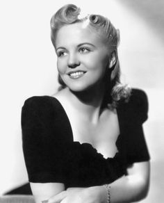 an old black and white photo of a woman with her arms crossed, smiling at the camera