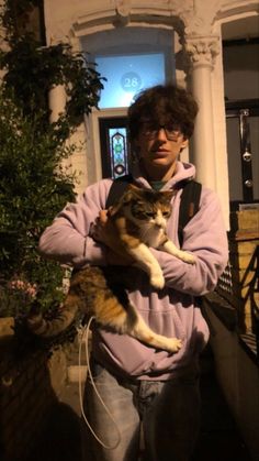 a man is holding a cat in his arms outside at night with the lights on