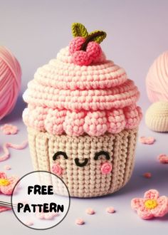 a crocheted cupcake with a pink frosting on top, surrounded by balls of yarn