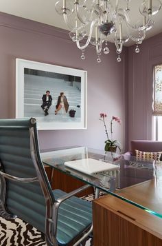 an office with purple walls and a chandelier hanging from the ceiling over a glass desk