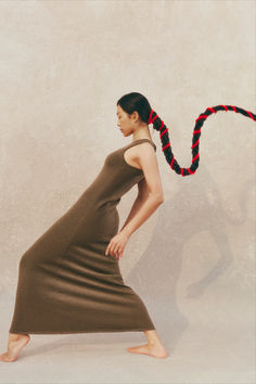 a woman in a long brown dress is holding a red and black rope around her neck