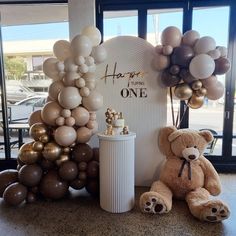 a teddy bear sitting next to balloons in front of a sign