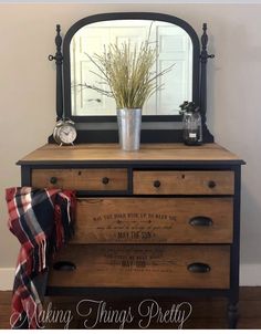 a dresser with a mirror and some plants on top, next to a plaid blanket