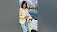 a woman standing next to a white car in front of a parking lot with her hand on the door handle