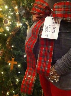 a pregnant woman wearing a red and green plaid ribbon around her belly with a christmas tree in the background