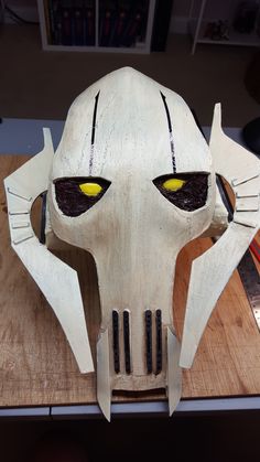 a white mask with yellow eyes on top of a wooden table