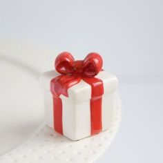 a red and white gift box with a bow on it's side sitting on a plate