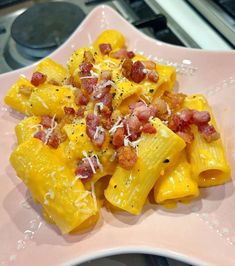 a pink plate topped with pasta covered in bacon and cheese on top of a stove