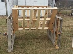 a wooden bed frame sitting in the middle of grass next to a fence and building