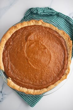 a pie sitting on top of a white table next to a green napkin and blue checkered cloth