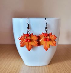 a pair of earrings with orange and red leaves on them sitting in front of a white bowl