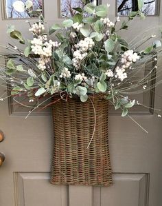 a wicker basket with white flowers and greenery hanging on the front door handle