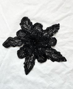 a black lace flower is on a white sheet with sequins in the center