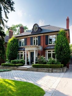 a large red brick house with black shutters on the front and side windows, surrounded by greenery