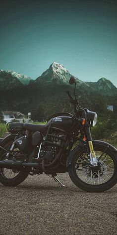 a black motorcycle parked on the side of a road with mountains in the back ground