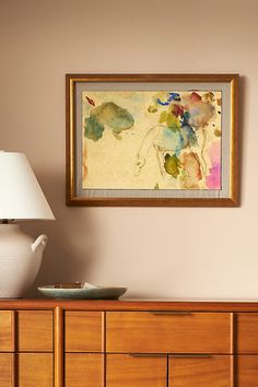 a painting hanging on the wall above a dresser with a lamp in front of it