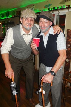 two men standing next to each other with canes in their hands and one holding a cup