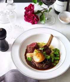 a white plate topped with meat and veggies next to a glass of wine