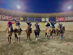 five men in sombreros are riding horses at an arena with their arms up