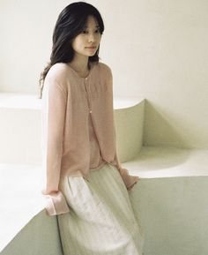 a woman standing next to a white wall wearing a pink sweater and skirt with her hands on her hips