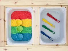 two plastic trays filled with sand and spoons on top of a wooden table