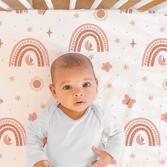 a baby laying on top of a bed next to a pink and gold wallpaper