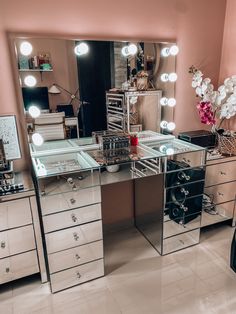 a mirrored vanity with lights on it in a pink room next to a dresser and mirror