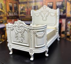 a white bed with ornate carvings on the headboard and foot board in front of a wallpapered background