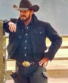 a man wearing a cowboy hat standing next to a wooden fence with his hands on his hips