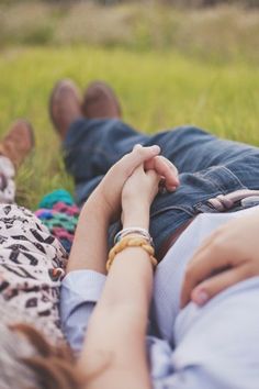 two people holding hands while laying in the grass