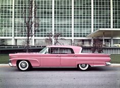 an old pink car is parked in front of a large building with glass windows on it