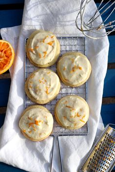 orange cookies with icing on a cooling rack next to an orange slice and whisk