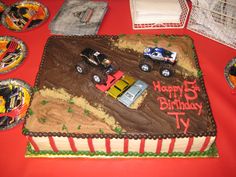 a birthday cake decorated with cars and trucks on a red tableclothed table cloth