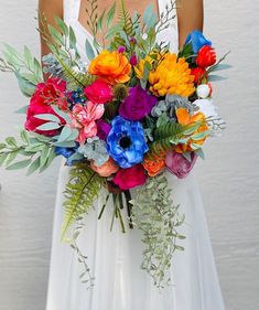 a woman in a white dress holding a bouquet of colorful flowers and greenery on her wedding day