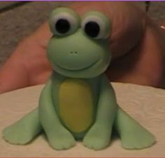 a frog cake sitting on top of a table next to a person's hand