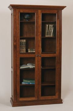 a wooden bookcase with two glass doors and books on the bottom shelf, in front of a white wall