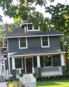 a gray house with white trim on the front porch and two story dormer windows