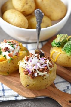 three baked potatoes with meat and vegetables in the middle on a cutting board next to a bowl of broccoli