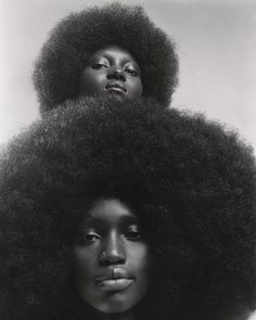 two women with large afros on their heads, one is looking at the camera