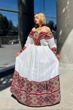 a woman in a white and red dress is standing on the sidewalk with her hand on her hip