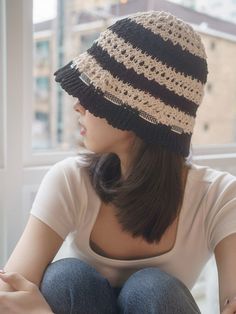 a woman sitting on a window sill wearing a hat with crocheted stripes