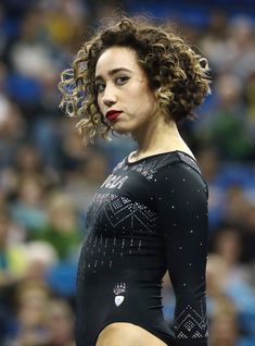 a woman with curly hair standing in front of a crowd wearing a black shirt and holding a tennis racquet