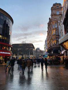 people are walking down the street in front of some buildings and shops at dusk or dawn