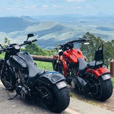 two motorcycles parked next to each other on the side of a road with mountains in the background