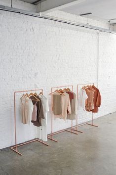 three racks with clothes hanging on them in front of a white brick wall and concrete floor