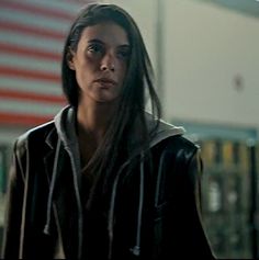 a woman with long hair standing in front of an american flag and looking at the camera