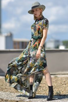 a woman in a dress and hat is walking on the ground with her legs crossed