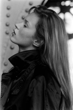 a woman with long hair standing in front of a wall and looking up at something